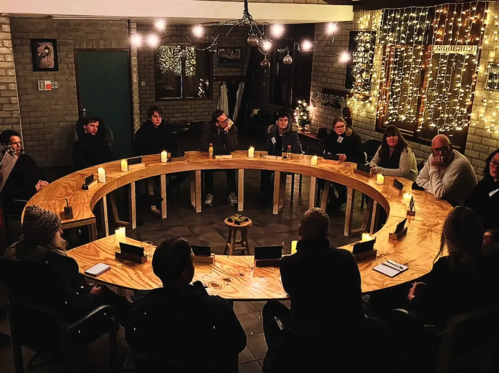 De volledige groep rond de ronde raadstafel bij kaarslicht en kerstverlichting